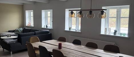 A modern living room with a dining area, a sofa set, and a large window with daylight.