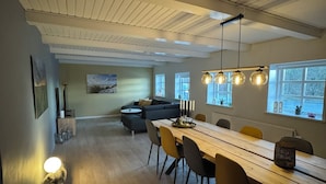 Et moderne spiseområde med et langt træbord, flere stole og hængende lamper.