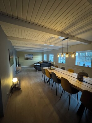 Ett modernt matområde med ett långt träbord, flera stolar och hängande lampor.