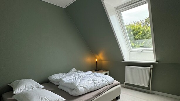 Et soveværelse med en enkelt seng, et natbord, en lampe, et vindue og en radiator.