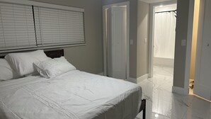 A bedroom with a bed, white curtains, and a door leading to a bathroom. - Waterfront getaway, relaxation done right here (Fort Myers)