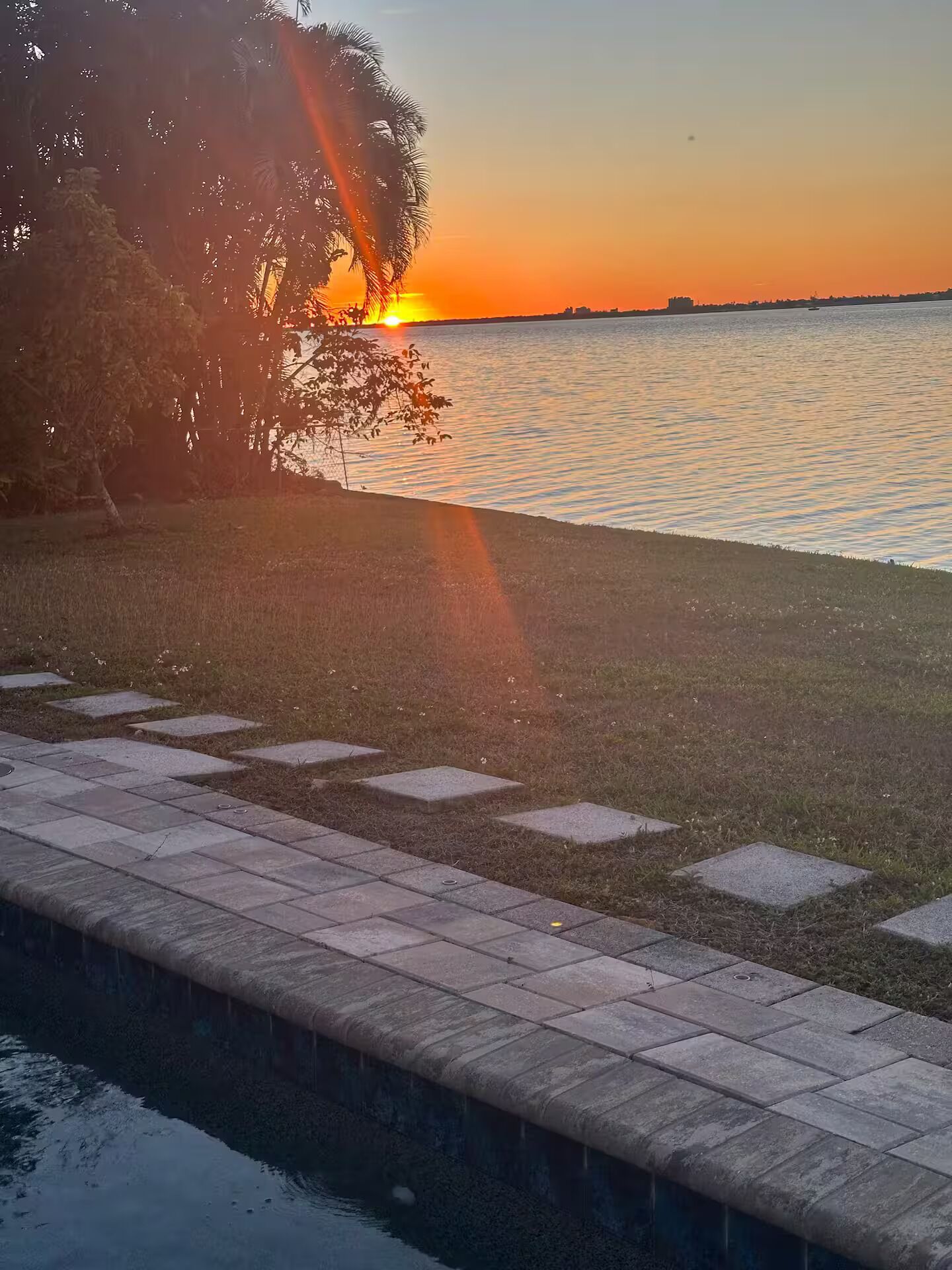 A sunset view over a body of water with a grassy area and a paved walkway.