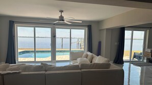 A modern living room with a sectional sofa, a ceiling fan, and large sliding glass doors leading to a pool and a view of the water. - Waterfront getaway, relaxation done right here (Fort Myers)