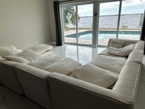 A spacious living area with a large beige sectional sofa, a glass sliding door leading to a pool, and a view of the water. - Waterfront getaway, relaxation done right here (Fort Myers)