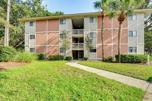 A multi-story building with a central entrance, surrounded by a well-maintained lawn and palm trees. - Unwind Poolside, Walk to Beach! Tennis, Pickleball (Hilton Head Island)