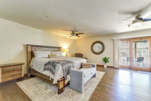 Ein Schlafzimmer mit einem Bett, Nachttischen, einem Deckenventilator, einem großen Spiegel und Blick durch eine Schiebetür zu einem Außenbereich.