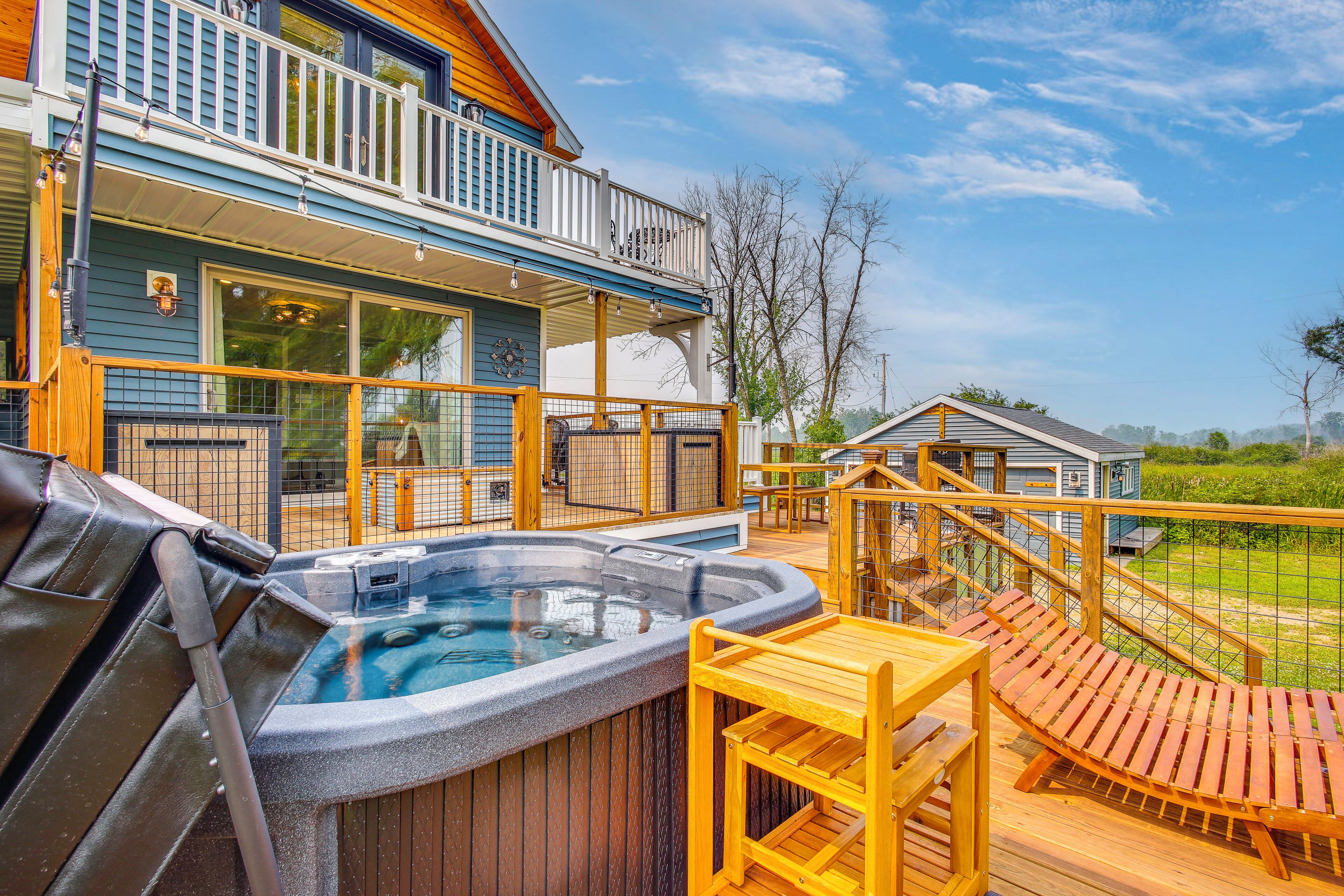 Un jacuzzi en una terraza de madera con vista a una casa y un patio cercado.