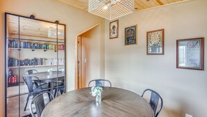A dining area with a round table, chairs, a bookshelf, and framed pictures on the wall. - Bayfront Home! Dock, Deck, Hot Tub, & Fire Pit (Oconto)
