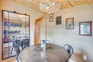 A dining area with a round table, chairs, a bookshelf, and framed pictures on the wall. - Bayfront Home! Dock, Deck, Hot Tub, & Fire Pit (Oconto)