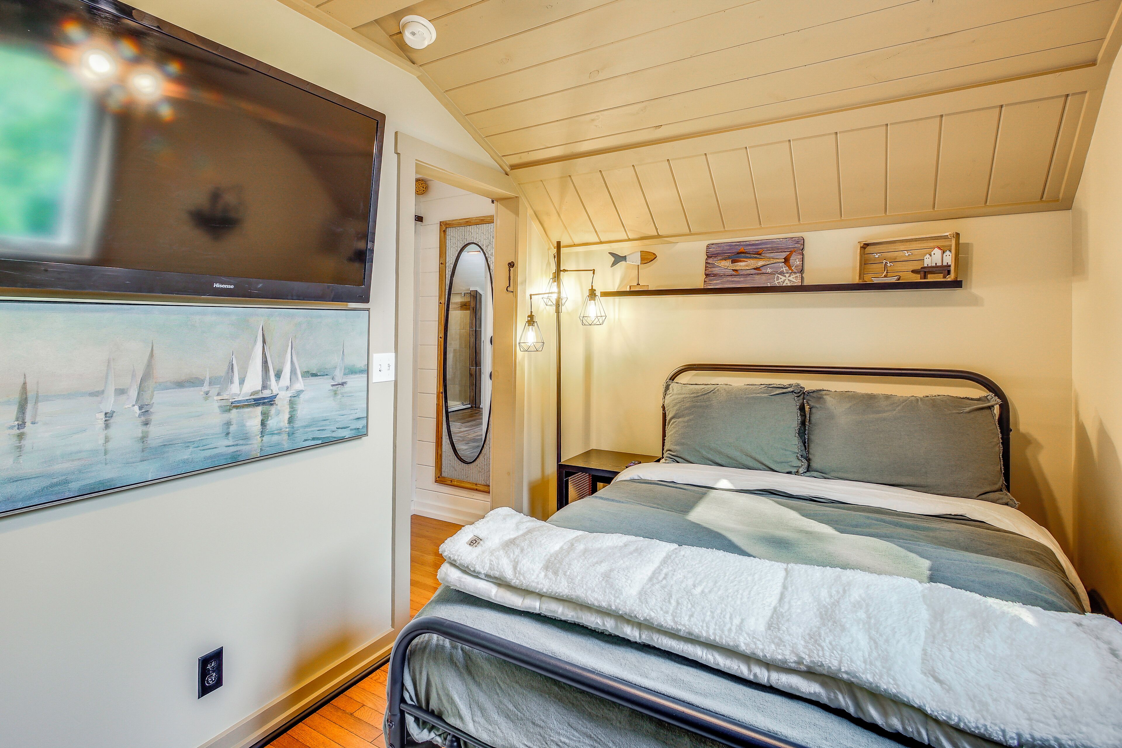 Un dormitorio con cama, un cuadro de veleros, un espejo y una estantería con objetos decorativos.