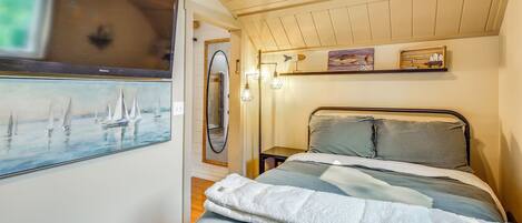 A bedroom with a bed, a painting of sailboats, a mirror, and a shelf with decorative items.