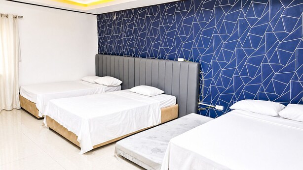 Een hotelkamer met drie bedden, een grijs hoofdeinde en een blauwe wand met een geometrisch patroon.