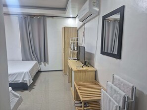 Habitación de hotel con cama, escritorio con computadora, radiador y ventana con cortinas.