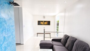 Een moderne woonkamer met een grijze bank, een glazen salontafel en een schilderij aan de muur.