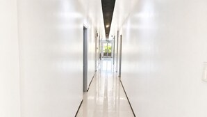 A long, straight corridor with white walls and a shiny floor, leading to a bright exit.