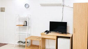 Een compacte kamer met een bureau, een televisie, een plank met een waterkoker, en een kleine koelkast.