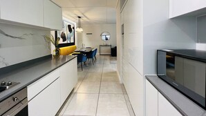 A modern kitchen with white cabinetry, a black countertop, and a dining area with blue chairs. - Luxurious 3-bedroom Apartment in Johannesburg's Waterfall Area (Johannesburg)