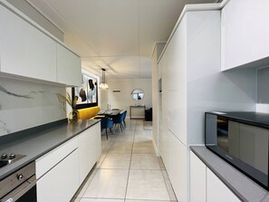 A modern kitchen with white cabinetry, a black countertop, and a dining area with blue chairs. - Luxurious 3-bedroom Apartment in Johannesburg's Waterfall Area (Johannesburg)