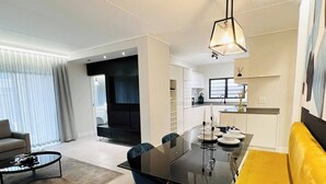 A modern living room with a dining table, blue chairs, a yellow sofa, and a black coffee table. - Luxurious 3-bedroom Apartment in Johannesburg's Waterfall Area (Johannesburg)