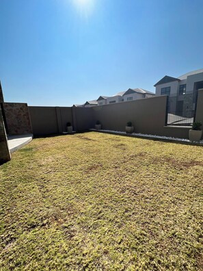 A rooftop with a grassy area, a stone wall, and a metal fence. - Luxurious 3-bedroom Apartment in Johannesburg's Waterfall Area (Johannesburg)