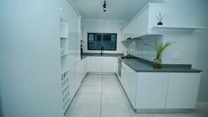 A modern kitchen with white cabinetry, a window, and a vase with greenery on the countertop. - Luxurious 3-bedroom Apartment in Johannesburg's Waterfall Area (Johannesburg)