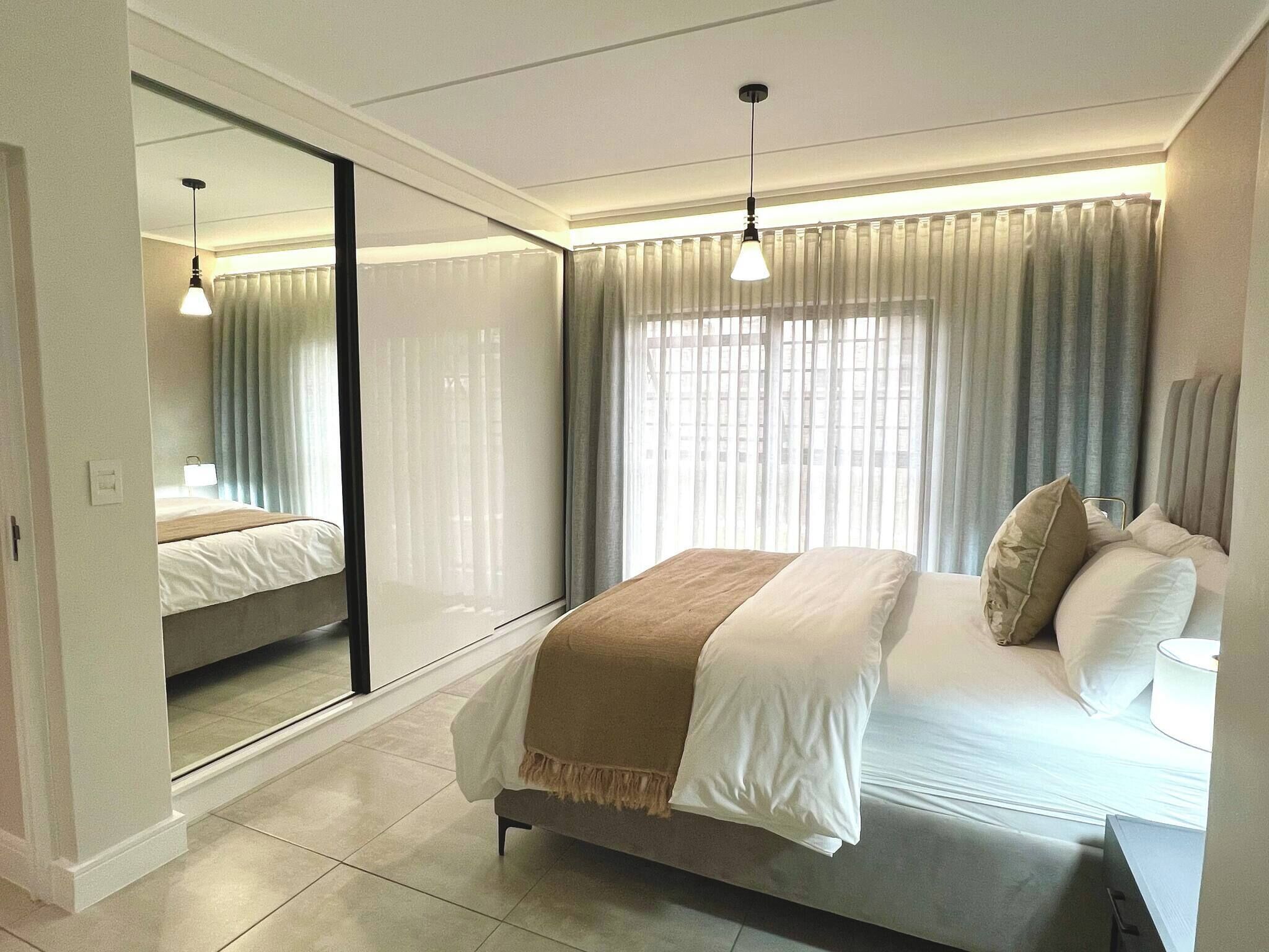 Un dormitorio moderno con una cama grande, una mesita de noche, un espejo y una ventana con cortinas.