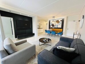 En moderne stue med et fladskærms TV, en sofa, et sofabord og et spiseområde med stole og et bord.