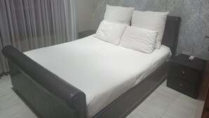 A neatly made bed with white bedding, a dark headboard, and a small bedside table with a lamp. - Luxurious 4-Bedroom House Rental with Pool Access in Ngaka Modiri Molema (Ngaka Modiri Molema District Municipality)
