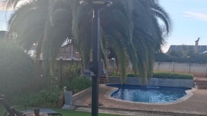 A backyard with a swimming pool, a lawn chair, a table, and a lamp post. - Luxurious 4-Bedroom House Rental with Pool Access in Ngaka Modiri Molema (Ngaka Modiri Molema District Municipality)
