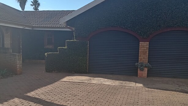 A residential property with a paved driveway, a garage with a closed shutter, and a brick wall. - Luxurious 4-Bedroom House Rental with Pool Access in Ngaka Modiri Molema (Ngaka Modiri Molema District Municipality)