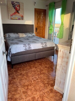 A bedroom with a bed, a door, a window with curtains, and a wall-mounted painting. - Casa Czuberny – Holiday Retreat (VC)