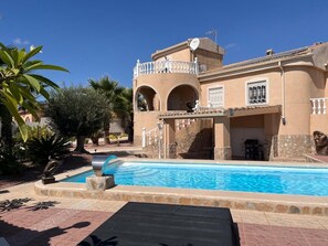 Ein Pool mit Liegeinsel, eine überdachte Terrasse und ein Gebäude mit Bögen und einem Balkon.