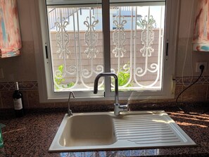 A kitchen sink with a faucet, a window with decorative metal bars, and a bottle of wine on the counter. - Casa Czuberny – Holiday Retreat (VC)