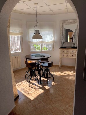 A dining area with a round table and four chairs, a hanging light fixture, a window with decorative iron bars, and a mirror with a decorative frame. - Casa Czuberny – Holiday Retreat (VC)
