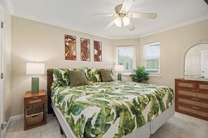 A bedroom with a bed, a nightstand, a dresser, a ceiling fan, and wall art. - Seascape Beachfront Condo w/Pool & Beach Views (Galveston)