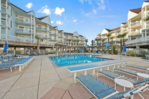 Ein Hotel mit Schwimmbad, Liegestühlen und einem überdachten Bereich mit Sonnenschirmen.