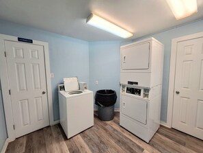 A laundry room with a front-loading washer and dryer, a trash can, and a door labeled 'STORAGE.' - Seascape Beachfront Condo w/Pool & Beach Views (Galveston)