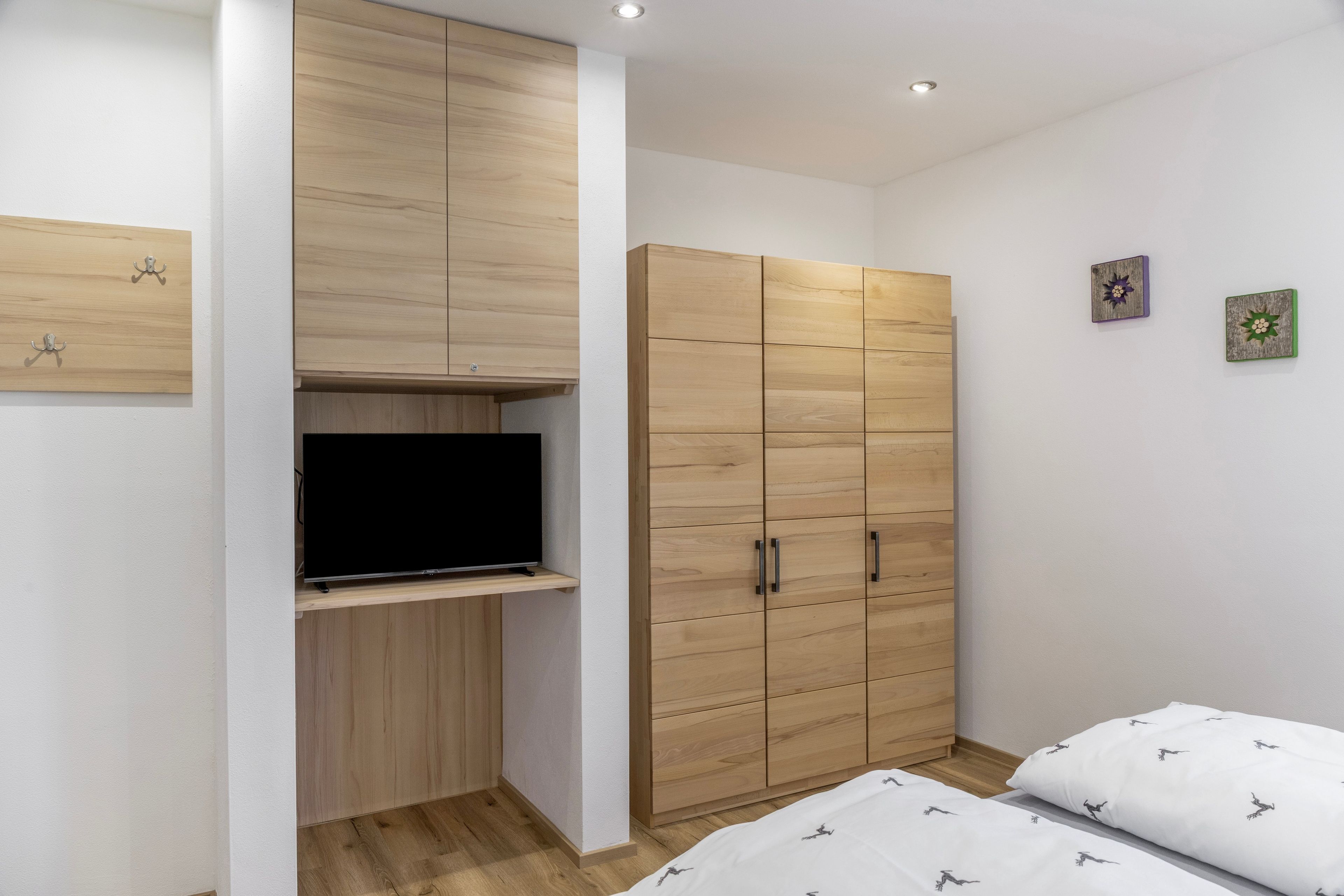 Een slaapkamer met een televisie op een plank, een houten garderobe, twee bedden en een kleine decoratie aan de muur.
