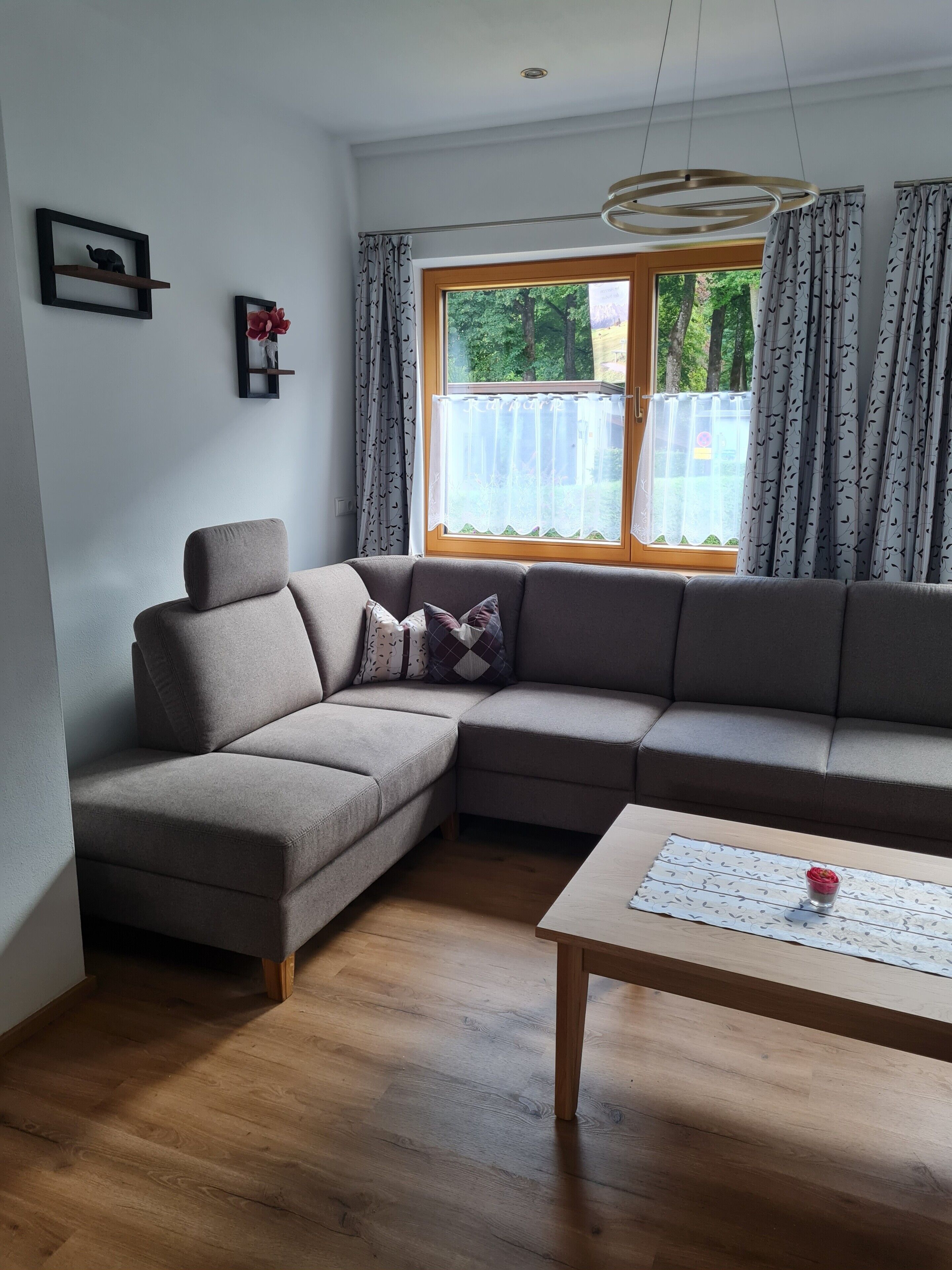 Una sala moderna con un sofá modular, una mesa de centro de madera y un ventanal con cortinas.