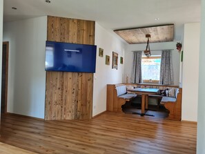 A modern living room with a wooden accent wall, a flat-screen TV, a dining area with a bench, and a ceiling with exposed beams. - Apartment "Karwendel" with Mountain View, Private Terrace and Wi-Fi (Mittenwald)