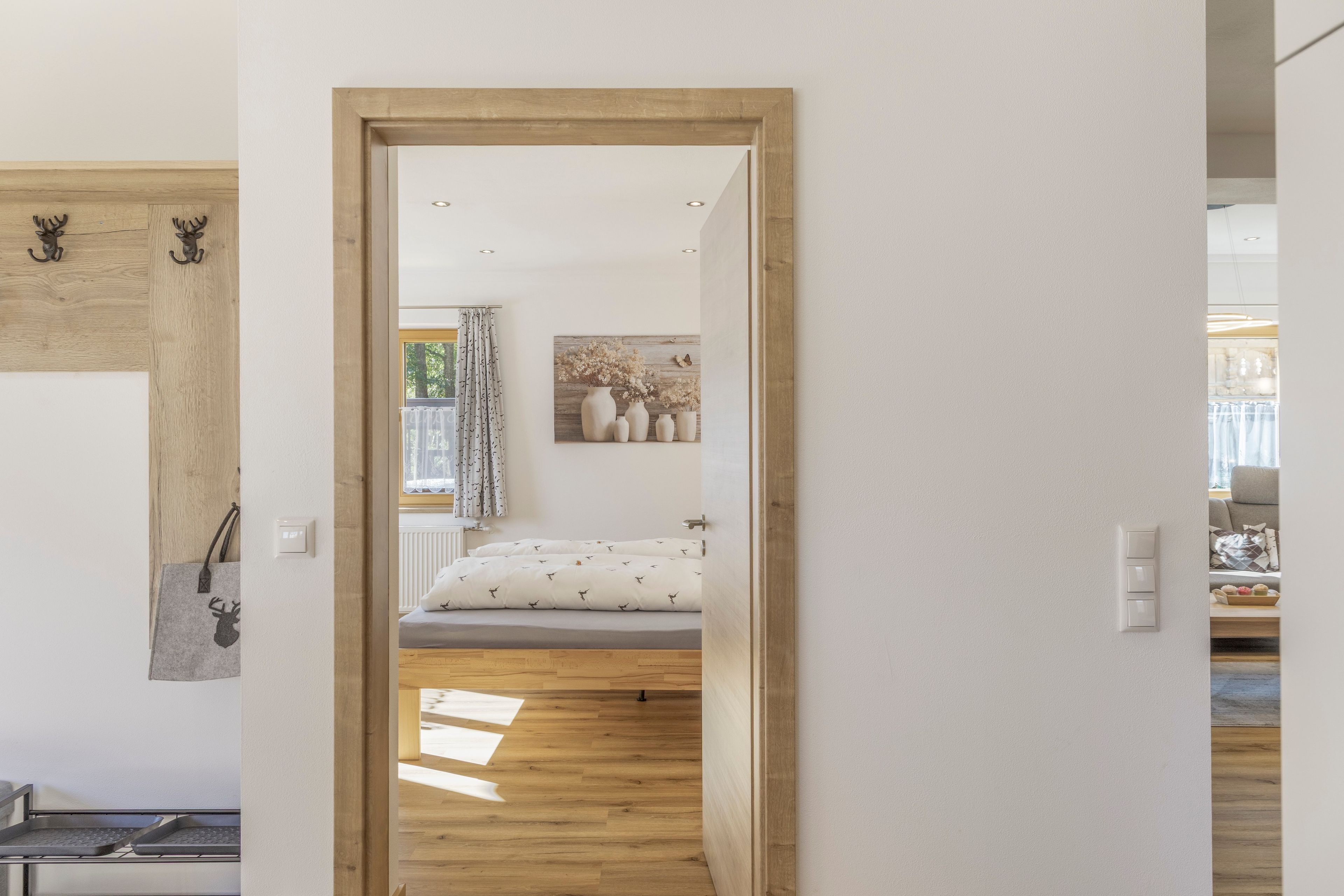 Une pièce avec un lit, un plancher en bois, un tableau au mur et une porte donnant sur une autre pièce.