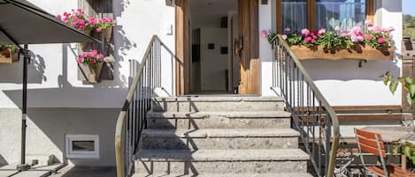 Un escalier menant à une porte en bois, avec des jardinières fixées aux murs et une table avec des chaises à l’extérieur.
