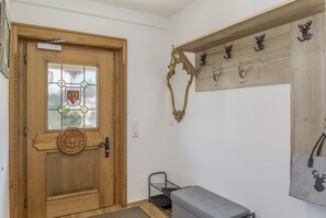 A wooden door with a glass panel and a coat of arms, a bench, a metal rack, and a wall-mounted coat rack with animal-shaped hooks. - Apartment "Karwendel" with Mountain View, Private Terrace and Wi-Fi (Mittenwald)