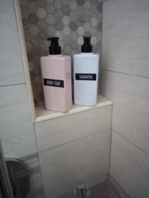 A bathroom with a shower area, a toilet, and a shelf with two bottles of body soap and shampoo. - alba magica (Agerola)