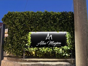 A sign for 'Alba Magica' with a hedge backdrop. - alba magica (Agerola)
