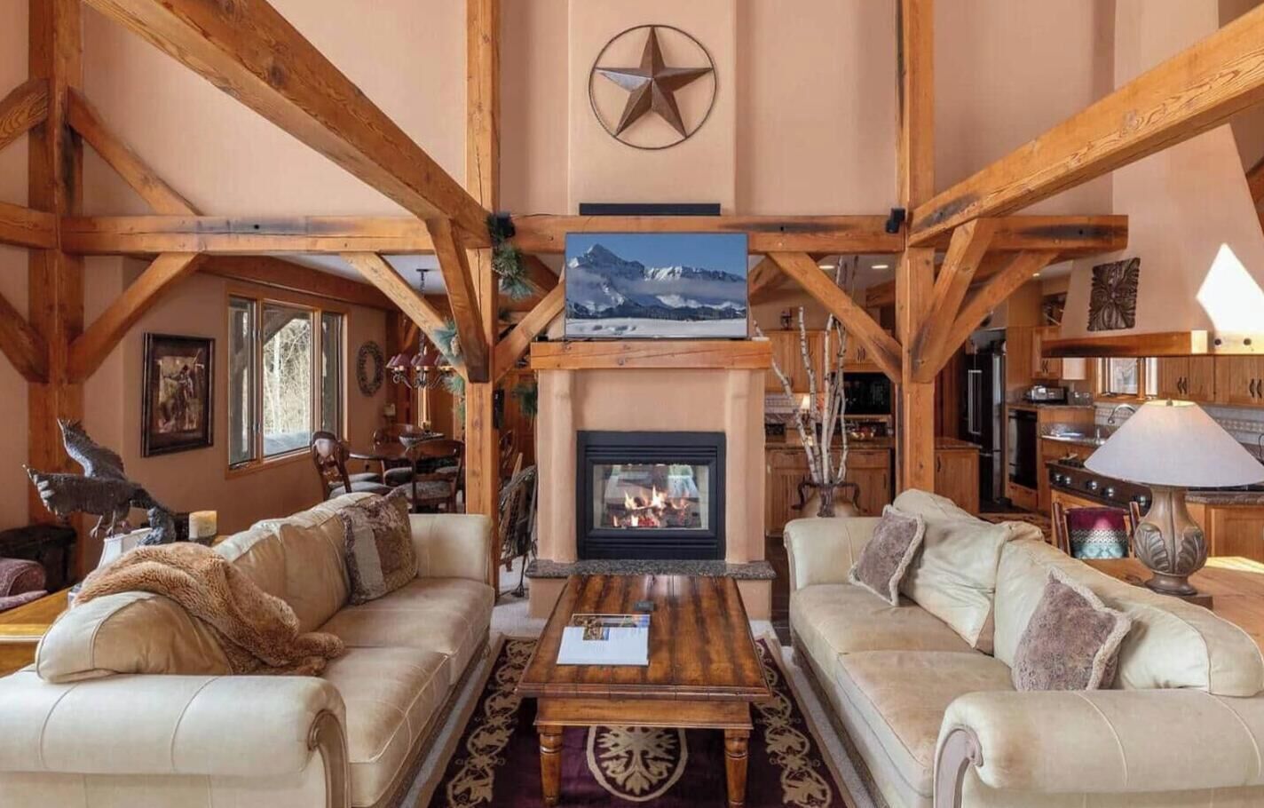 A spacious living room with a fireplace, wooden beams, and a large window.
