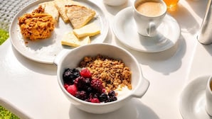 Ein Frühstücksbuffet mit Toast, Rührei, einer Beerenbowl, Granola und einer Tasse Kaffee auf einem Tisch.