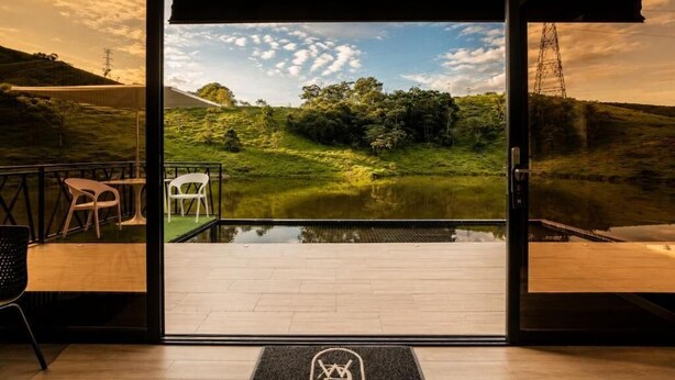 Ein Zimmer mit einer großen Glasdoor, die zu einer Wiese mit Teich, einer Holzterrasse und einem Stuhl führt.