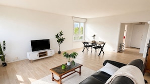 A modern living room with a flat-screen TV, a dining table with chairs, a sofa, and a coffee table. - Spacious, bright apartment with a balcony, 4 bedrooms (Mont-Saint-Aignan)