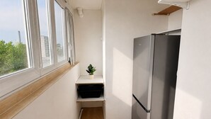A compact kitchen with a stainless steel refrigerator, a small plant on a shelf, and a window with curtains. - Spacious, bright apartment with a balcony, 4 bedrooms (Mont-Saint-Aignan)